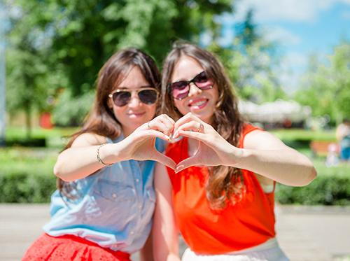 Two ladies make a heart image with their hands.